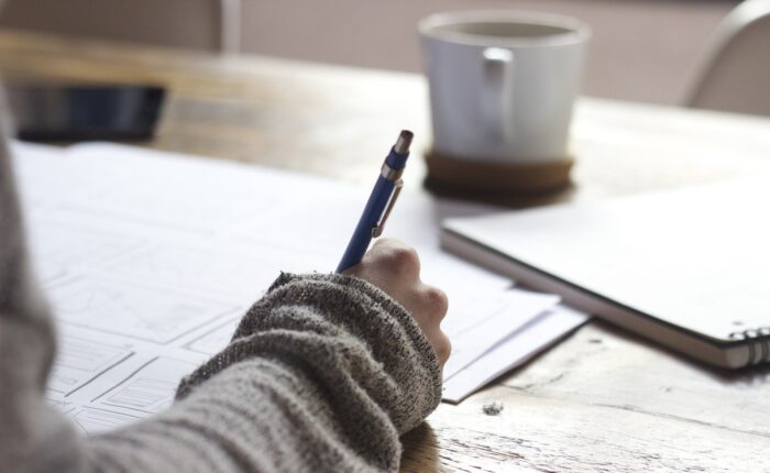 A person writing at a table with a cuppa. Source: Pixabay