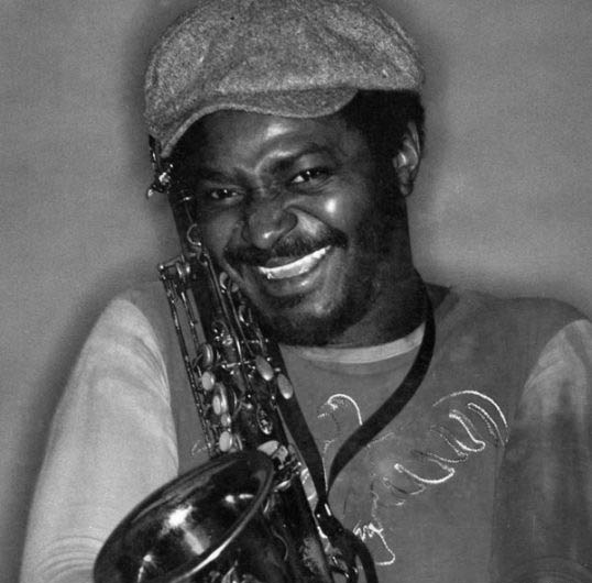 Pee Wee Ellis hugging his saxophone. A black and white photo. Image from https://secondhandsongs.com/artist/12536